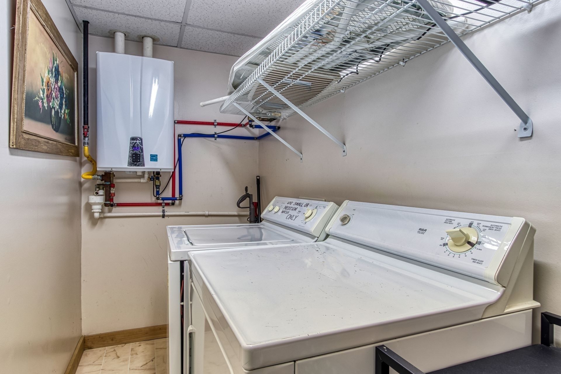 A laundry room with a white washing machine, a water heater, and a metal drying rack.