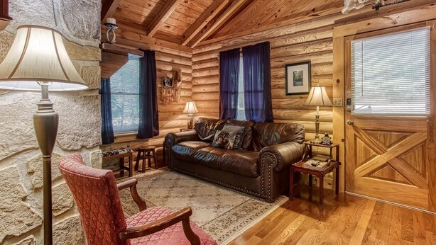 A log cabin interior with a leather sofa, two lamps, a rug, and a stone wall.