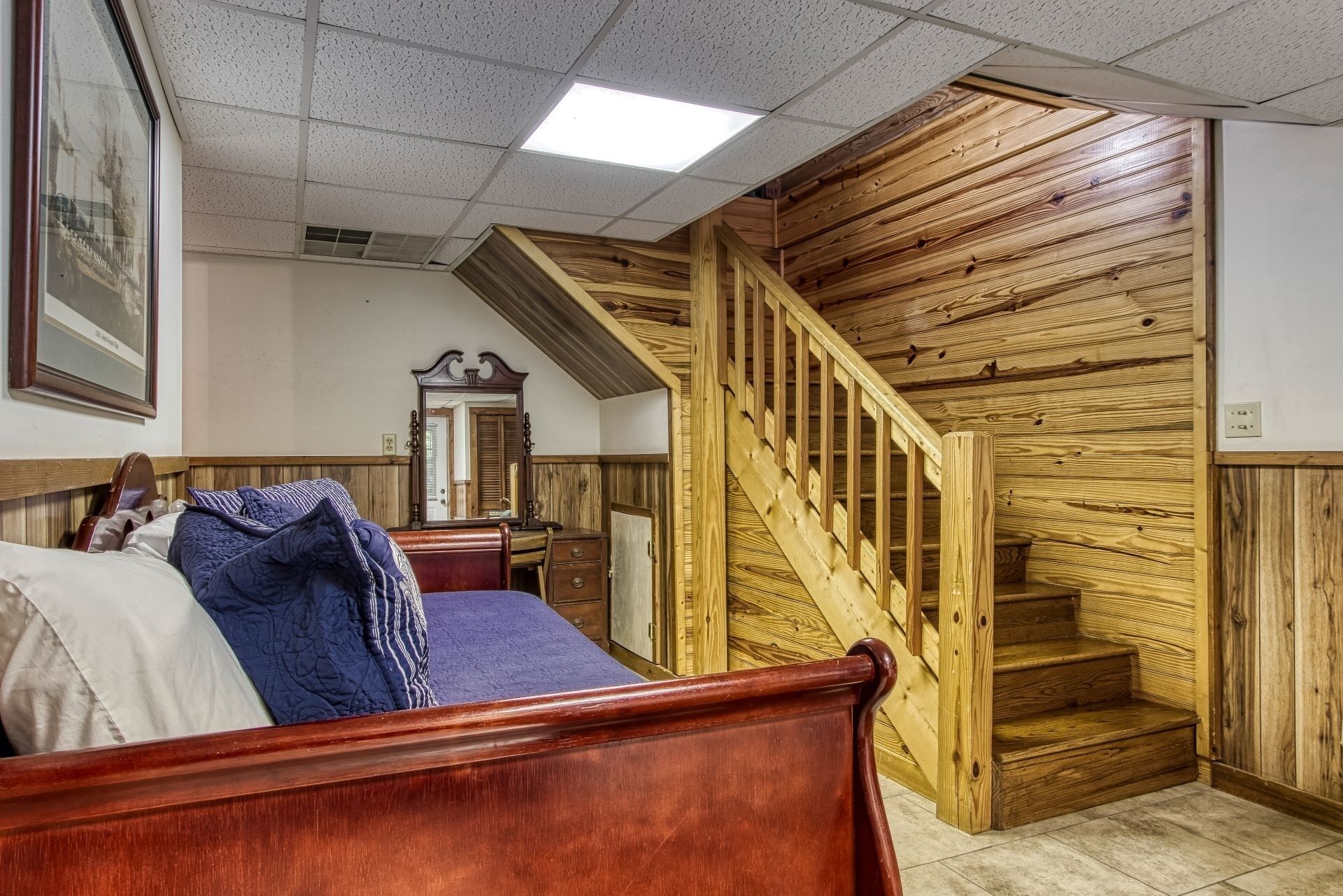A bedroom with a wooden staircase, a bed with a blue blanket, and a wooden headboard.