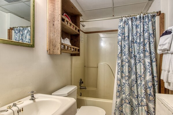 A bathroom with a shower curtain, a toilet, a sink, and a mirror. - Er44 - Rising Eagle - Great Location! Close To Town! 2 Bedroom Cabin by RedAwning (Pigeon Forge)