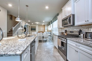 A modern kitchen with granite countertops, stainless steel appliances, and a dining area with white chairs.