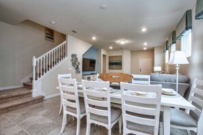 A dining area with a table set for four, a staircase, and a living room with a sofa and a lamp. - Brand New Family Getaway W/pool & Spa -7049sr 5 Bedroom Home by RedAwning (Davenport)