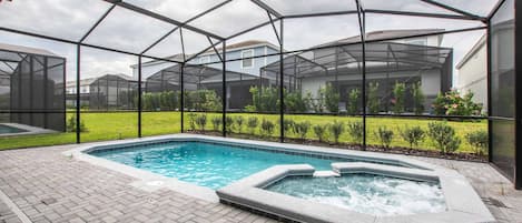 A swimming pool with a hot tub, surrounded by a covered patio area with a view of houses in the background.