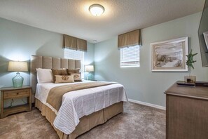 Un dormitorio con cama, lámparas de noche, mesita de noche, cómoda y un cuadro en la pared.