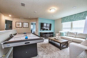 A living room with a pool table, a sofa, a coffee table, and a TV.