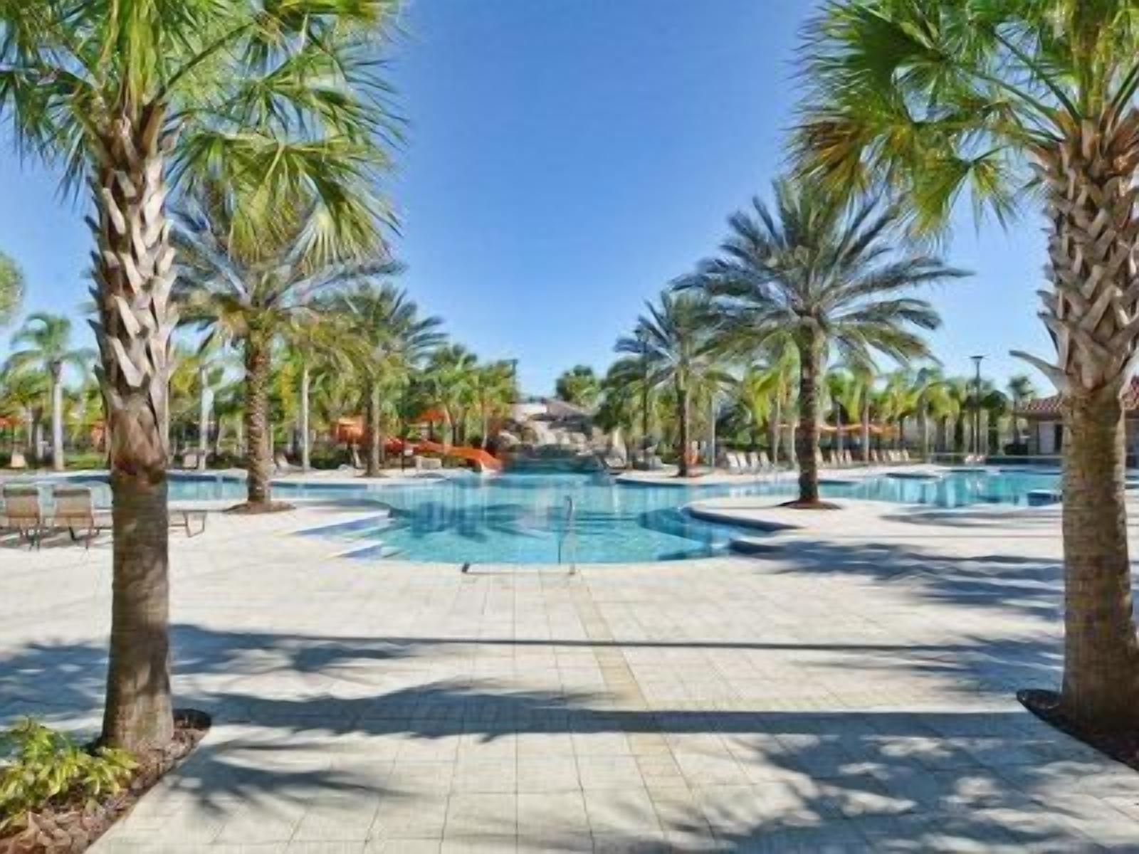 A pool area with palm trees, a clear sky, and a distant building.