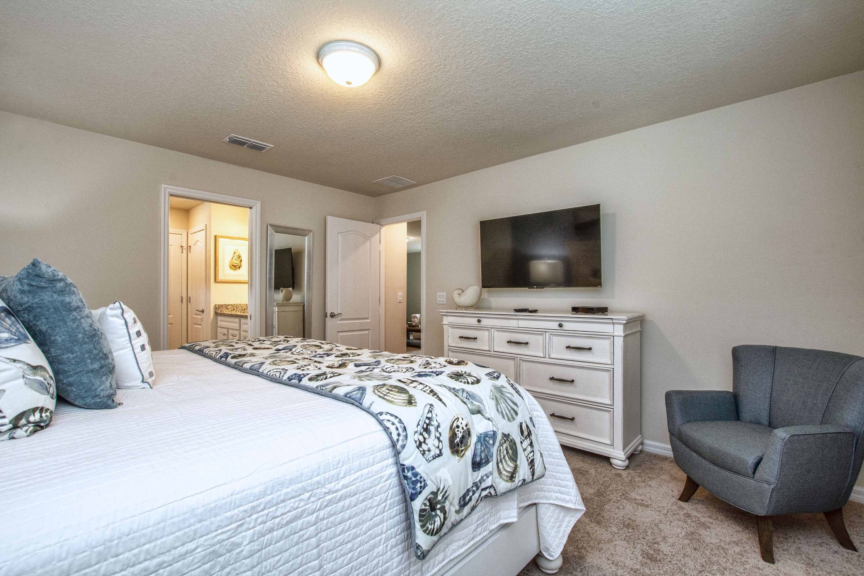A bedroom with a bed, dresser, chair, and a television on the wall.