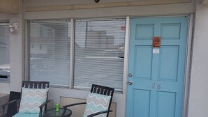 Une porte bleue avec un panneau « Il est interdit de fumer », deux chaises dotées de coussins à motifs et une petite table sur laquelle se trouve une boîte.