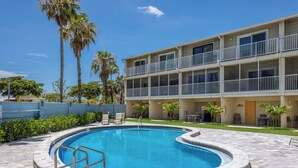 A two-story building with a swimming pool, outdoor seating, and palm trees. - Coastal 2BDRM Townhouse 100 Steps to Beach! (Holmes Beach)