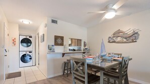 A compact kitchen with a dining area, a ceiling fan, and a wall-mounted artwork. - Coastal 2BDRM Townhouse 100 Steps to Beach! (Holmes Beach)