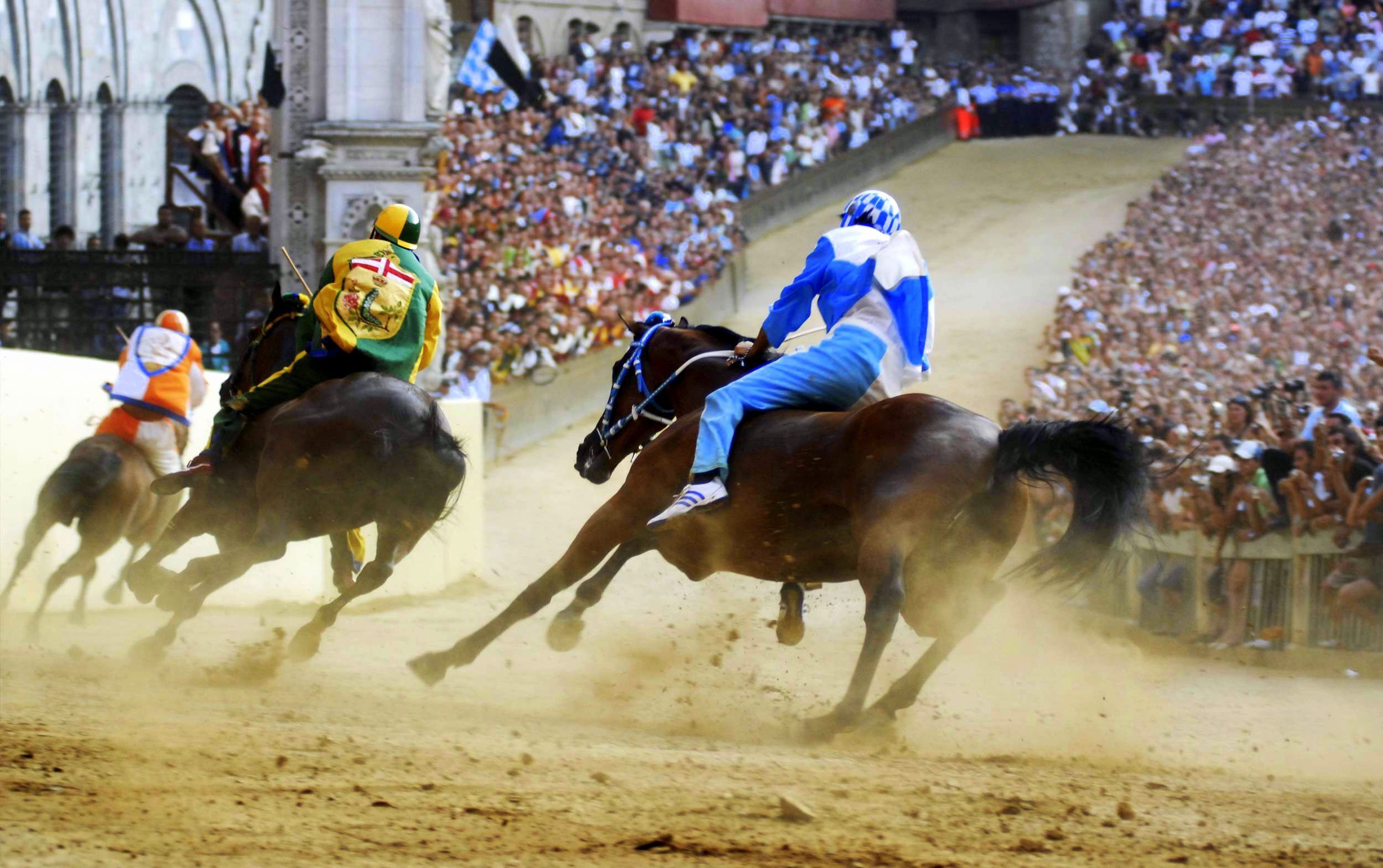 Et væddeløb med jockeys på heste, et publikum i baggrunden og en sandbane.
