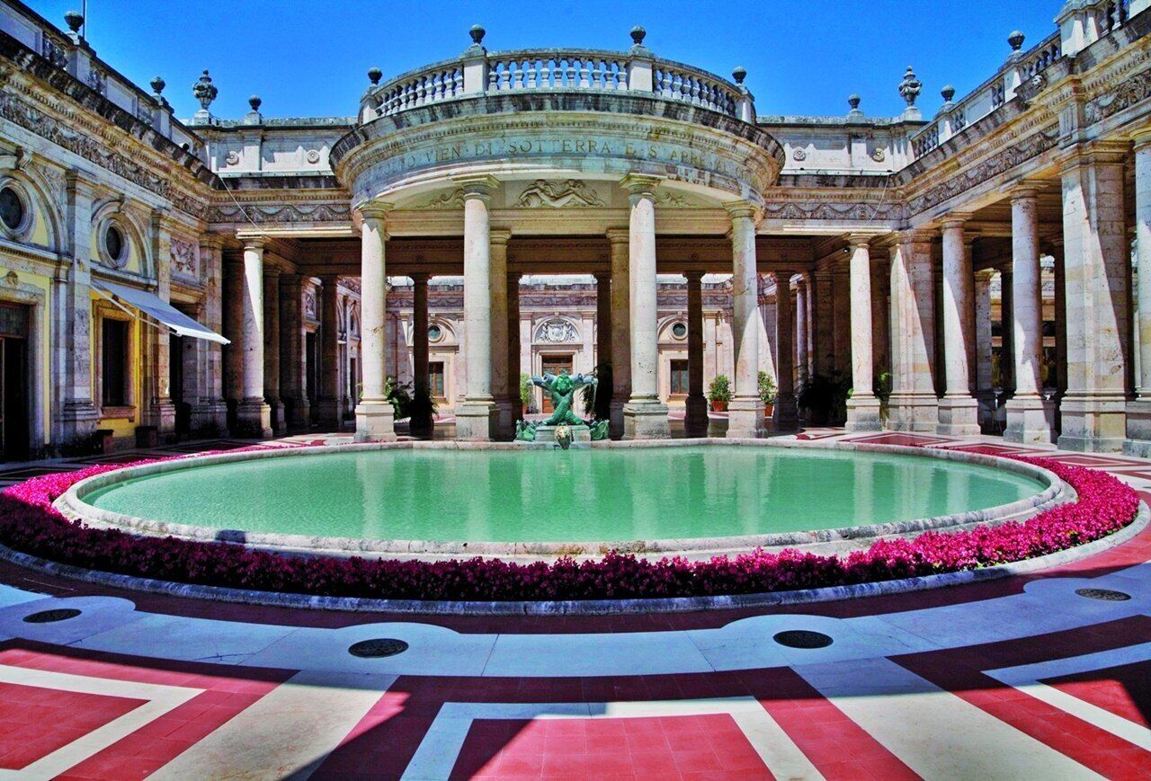 Un ampio cortile con una fontana al centro, circondato da colonne elaborate e una vasca circolare.