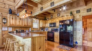 A wooden cabin-style kitchen with a large island, bar stools, a stainless steel refrigerator, and wooden cabinets. - Ern850 - Simply The Best - Great Location - Close To All The Action! 4 Bedroom Cabin by RedAwning (Pigeon Forge)