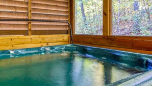 A wooden cabin with a hot tub and a window overlooking a forest.