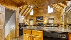 A wooden cabin interior with a kitchen, dining area, and living room.