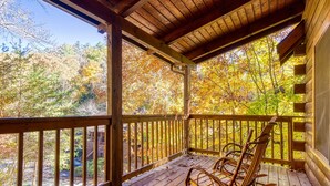 A wooden porch with rocking chairs, a wooden railing, and a view of autumn trees.