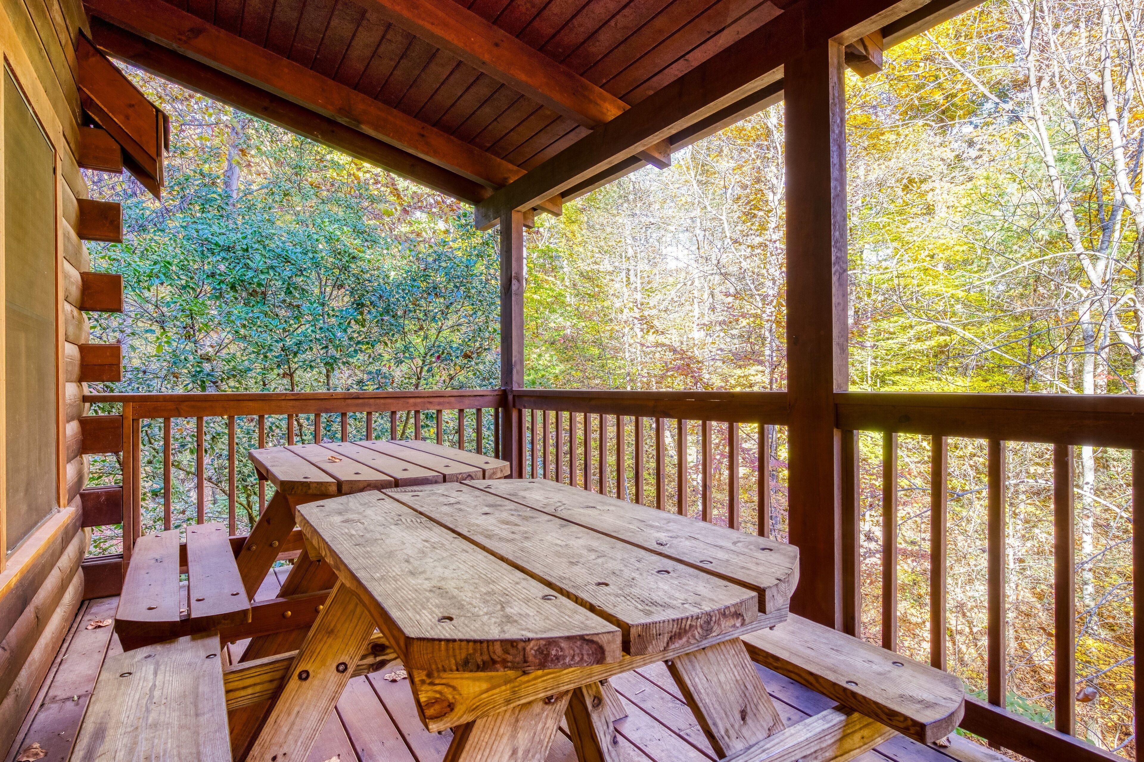 A wooden deck with picnic tables and a railing overlooking a forested area.