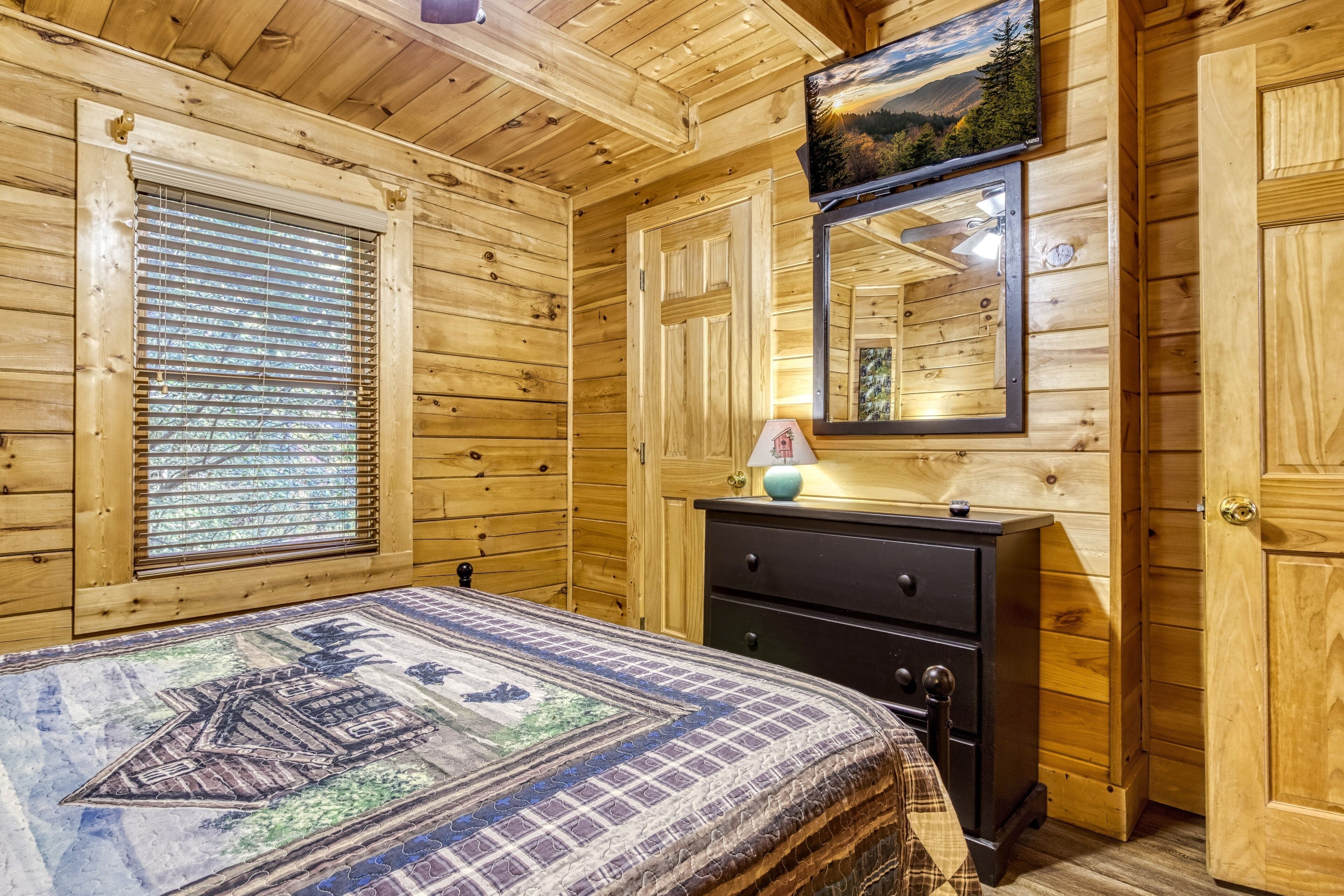 Quarto de cabana de madeira com cama, cômoda e uma janela grande com persianas.
