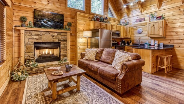 A cozy cabin interior with a stone fireplace, wooden walls, a brown leather sofa, a dining table, and a kitchen area. - Er260- Magical Moments Great Location- Close To Town 1 Bedroom Cabin by RedAwning (Pigeon Forge)