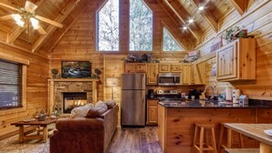 A cozy cabin interior with a stone fireplace, wooden furniture, a kitchen with modern appliances, and large windows offering natural light. - Er260- Magical Moments Great Location- Close To Town 1 Bedroom Cabin by RedAwning (Pigeon Forge)