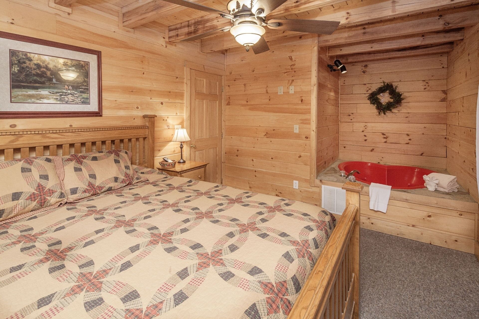 Habitación de cabaña de madera con una cama, una mesita de noche, una bañera roja y un ventilador de techo.