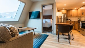 Une chambre d’hôtel moderne dotée d’une grande fenêtre, d’un téléviseur à écran plat, d’un lit, d’un coin repas et d’une kitchenette.