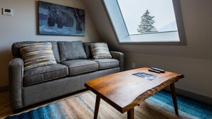 Un salon moderne avec un canapé gris, deux coussins à motifs, une table basse en bois et un tableau représentant un ours.