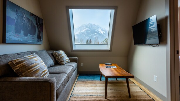 Un salon comprenant un canapé, une table basse, un téléviseur fixé au mur et une grande fenêtre donnant sur les montagnes.