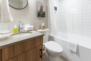 Bathroom features a large, curved bathtub, a wooden vanity, and a mirror with a round frame.