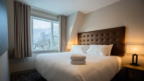 A hotel room with a large bed, a view of mountains, and a window with curtains. - Superior King Two Bedroom Apartment (Banff)