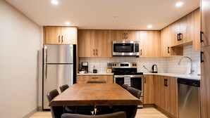 A modern kitchen with wooden cabinets, stainless steel appliances, and a dining table with chairs. - Superior King Two Bedroom Apartment (Banff)