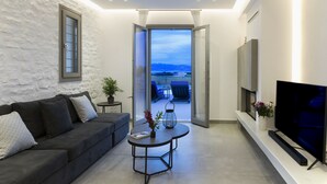 Un soggiorno moderno con divano, tavolino e televisore. Si vede un balcone con mobili da esterno attraverso la porta aperta.