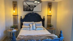 Un lit bien fait, recouvert d’une couvre-lit à motifs, avec deux tables de chevet de chaque côté, sur lesquelles sont posées des lampes et de petites plantes en pot.