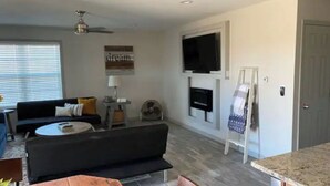 Un salon avec un canapé noir, une table basse, un téléviseur fixé au mur et une cheminée.