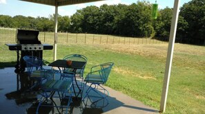 An outdoor patio with a grill, metal chairs, and a table.