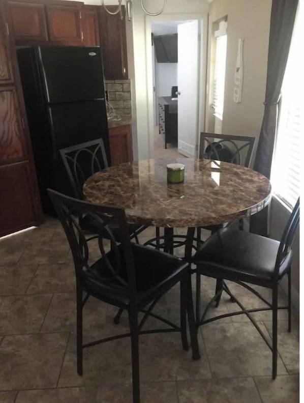 A kitchen with a round marble table, four chairs, and a black refrigerator.