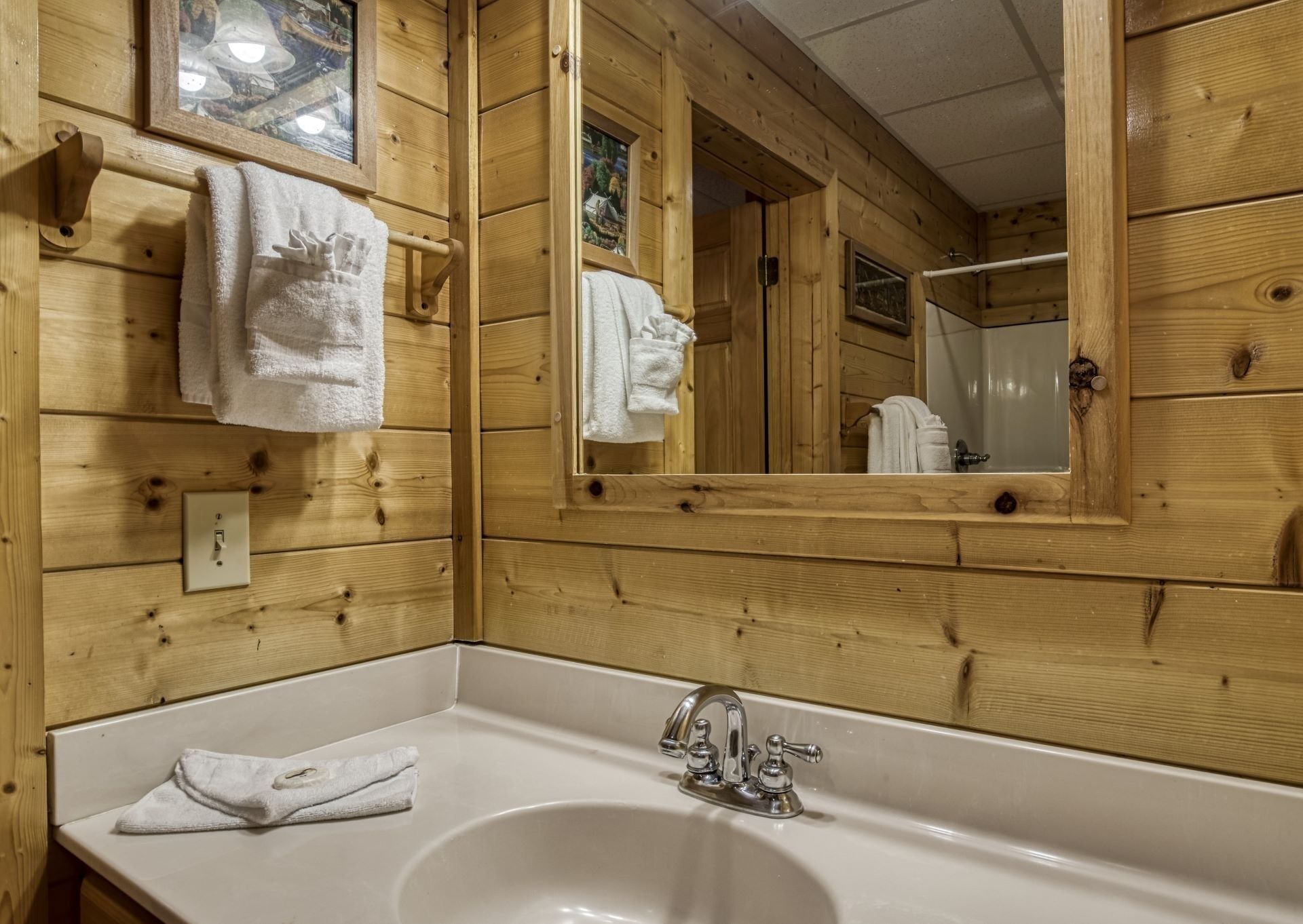 Un baño de cabaña de madera con un lavabo blanco, dos toallas colgadas en la pared y un espejo que refleja el cuarto.