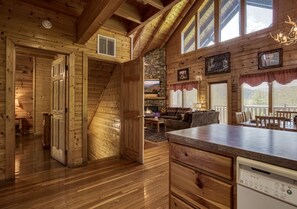 Ein Holzblockhaus-Interieur mit Küche, Essbereich und einer Treppe, die zu einer Schlafempore führt.