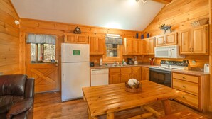 A wooden cabin with a kitchen featuring wooden cabinets, a refrigerator, a microwave, and a stove. There is a dining table with a basket of bread and a chair. - Er307- Eagle's View- Great Location- Close To Town 2 Bedroom Cabin by RedAwning (Pigeon Forge)