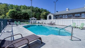 A swimming pool with lounge chairs and a gazebo in a fenced area, surrounded by trees and a building with a balcony.