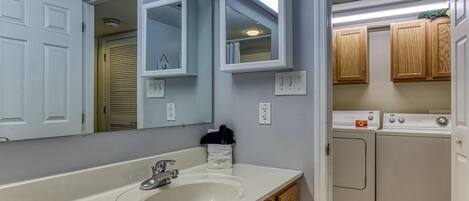 A bathroom with a sink, mirror, and wooden cabinets. There is a window with blinds and a light fixture above the mirror.