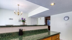 A kitchen with a granite countertop, wooden cabinets, a chandelier, and a clock on the wall.