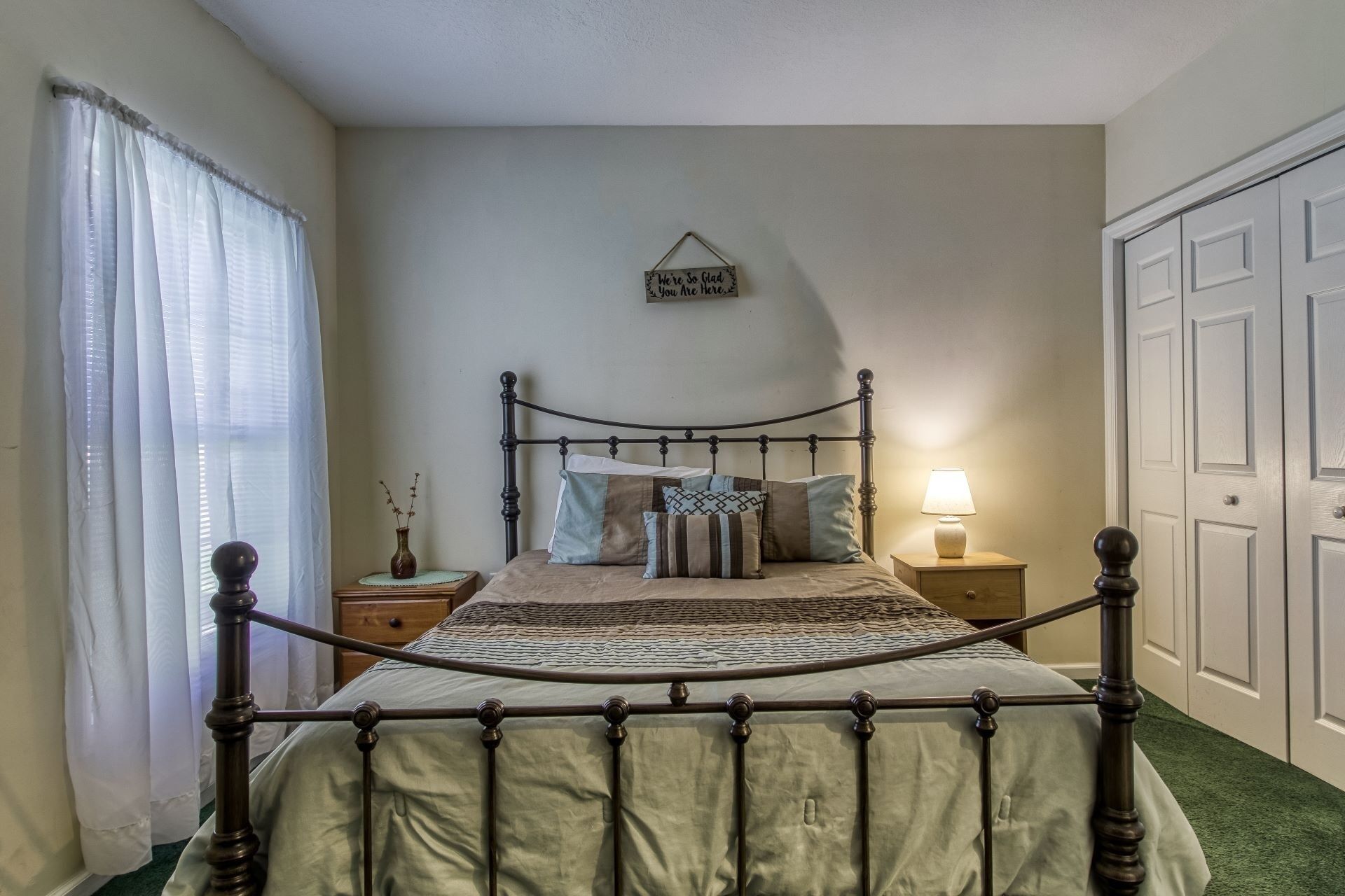 A bedroom with a four-poster bed, a bedside table with a lamp, a wall-mounted sign, and a door.