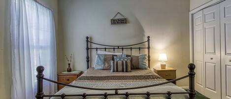 A bedroom with a four-poster bed, a bedside table with a lamp, a wall-mounted sign, and a door.