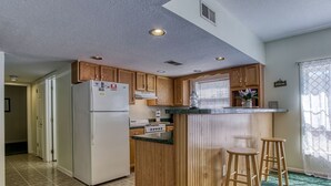 A compact kitchen with wooden cabinets, a refrigerator, a stove, and a small bar area with stools.