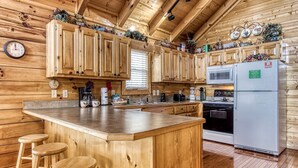 A wooden cabin kitchen with a central island, wooden bar stools, a microwave, a refrigerator, and a clock on the wall.