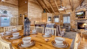 A wooden cabin interior with a dining table set with bowls and plates, a fireplace, and a television mounted on the wall.