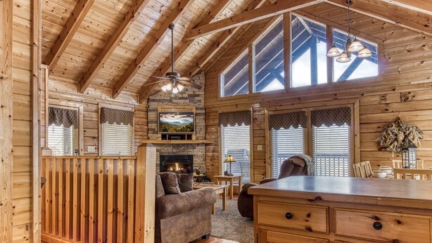 A cozy cabin interior with a fireplace, wooden furniture, and large windows.