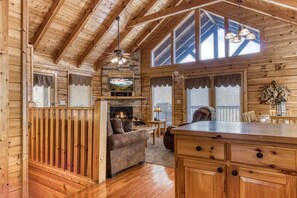 Interior acogedor de una cabaña con chimenea, muebles de madera y ventanas amplias.