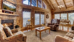 A cozy log cabin interior with a fireplace, comfortable seating, and large windows.